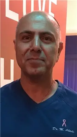 Dr. Moe Abtahi smiling in navy scrubs with a pink ribbon and his name embroidered on the chest